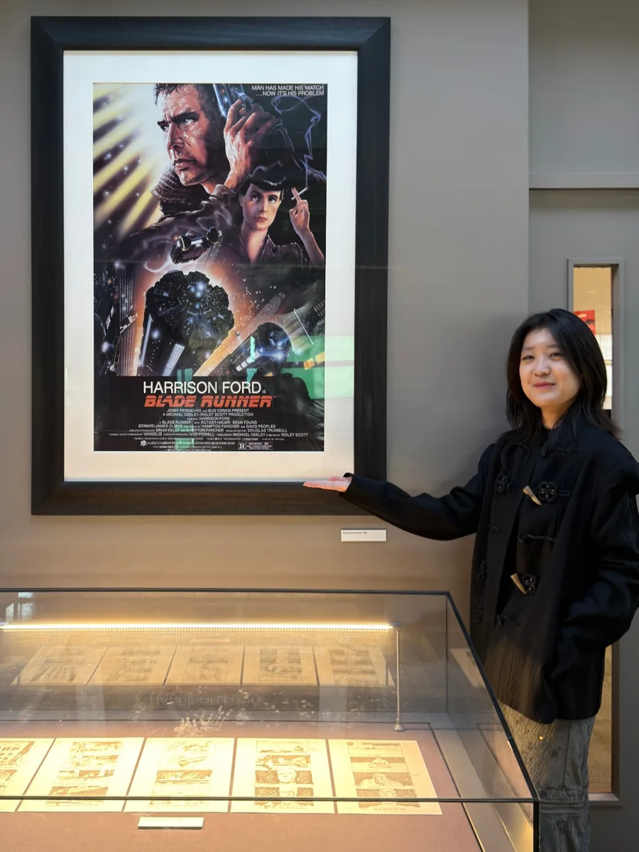 Mengdie Lu beside a framed Blade Runner poster in an exhibition.